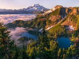 Breathtaking golden-hour wilderness landscape with a winding river, majestic mountain range, and lone backpacker overlooking the sunset vista