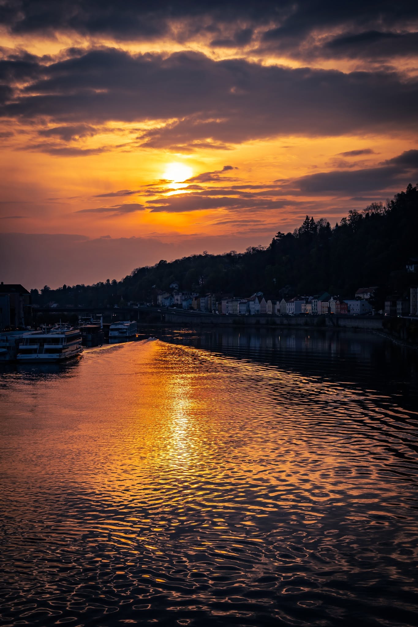 Passau Sonnenuntergang am Fluss — orange-goldenes Licht spiegelt sich auf der Donau mit Schiffen am Ufer