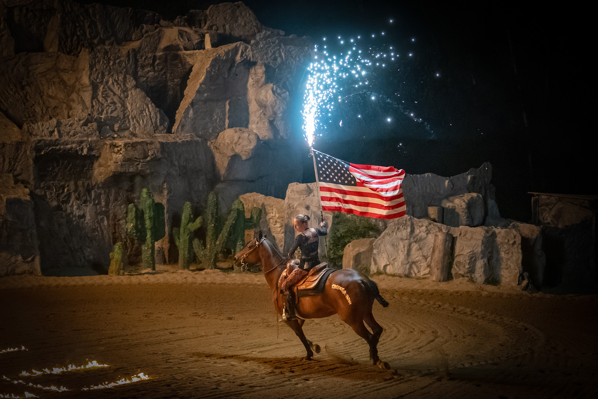 Pullman City Feuershow 2026 — Reiterin mit US-Flagge und Funkenregen in der Nachtshow