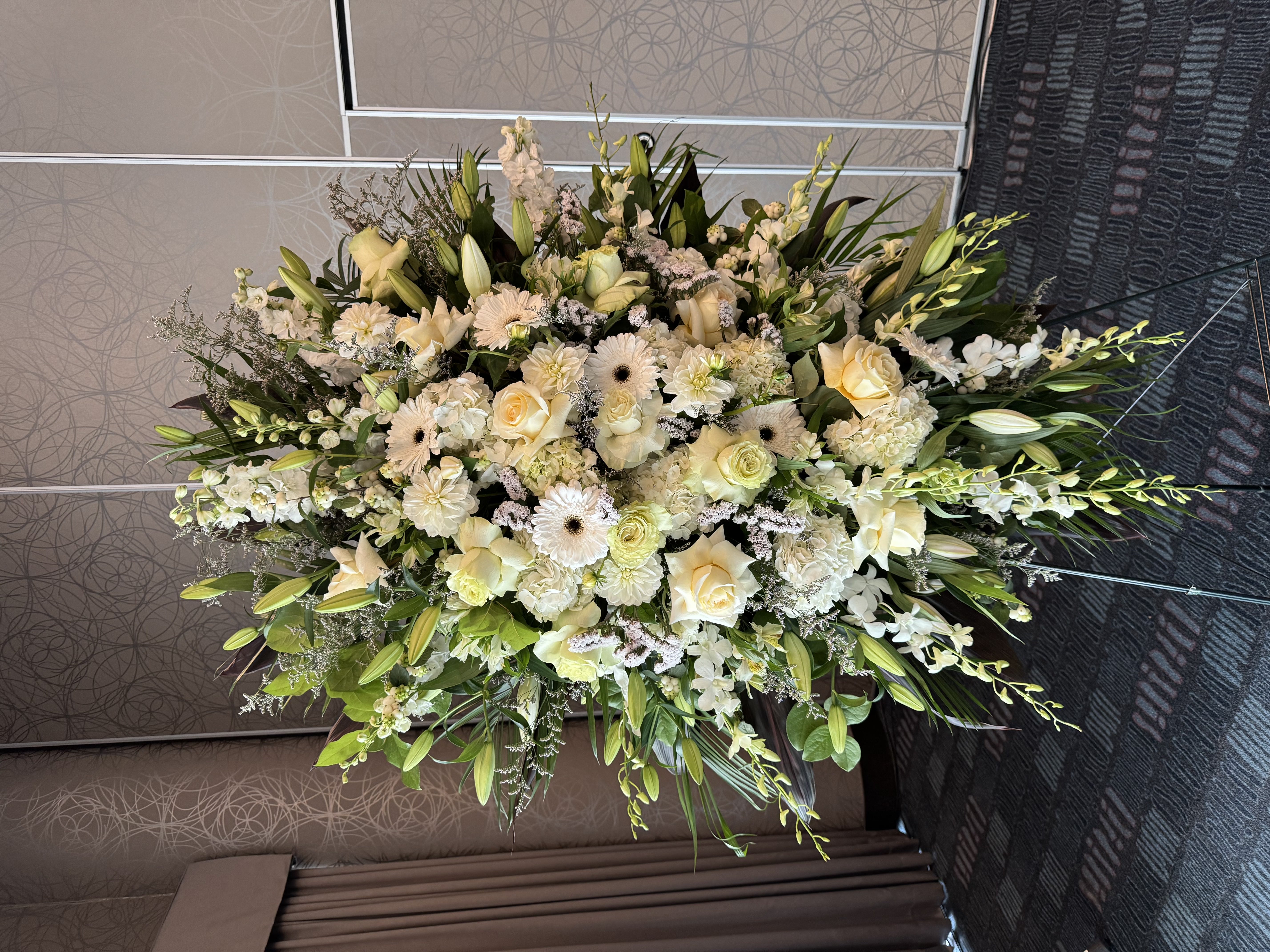 White lily and orchid cross-shaped funeral tribute with greenery