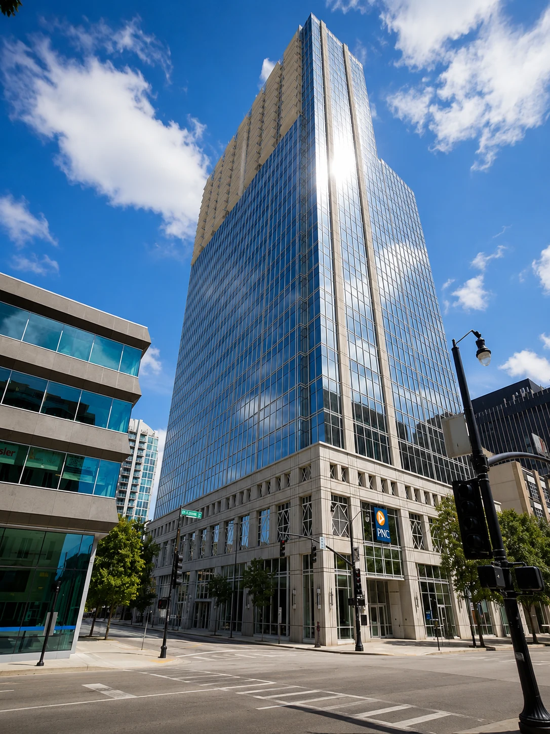 Fast Passport Center office at 301 Fayetteville St in downtown Raleigh — modern PNC Plaza glass tower with blue reflective curtain wall and stone base at the corner of Fayetteville Street and Davie Street