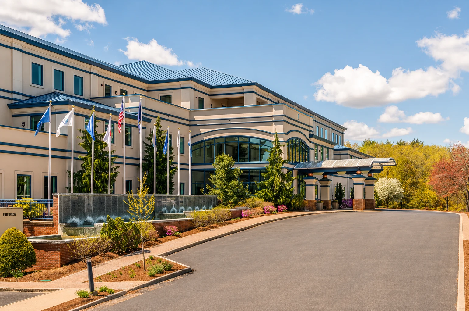 Fast Passport Center office building in Portsmouth, NH — modern multi-story facility with blue roof, landscaped entrance with fountain, and American flags near Pease International Tradeport