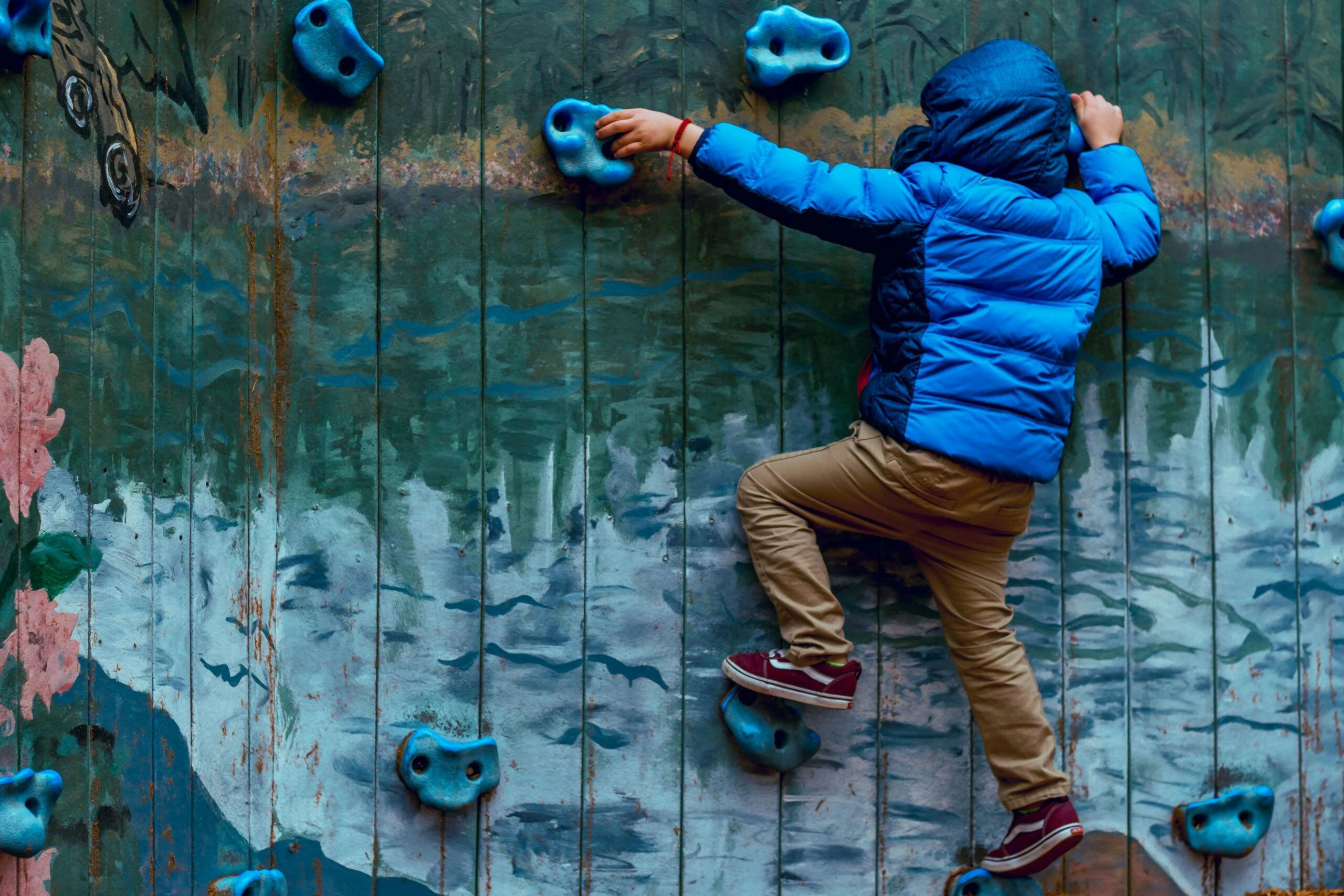 Child climbing a colourful climbing wall, demonstrating determination and reaching for potential