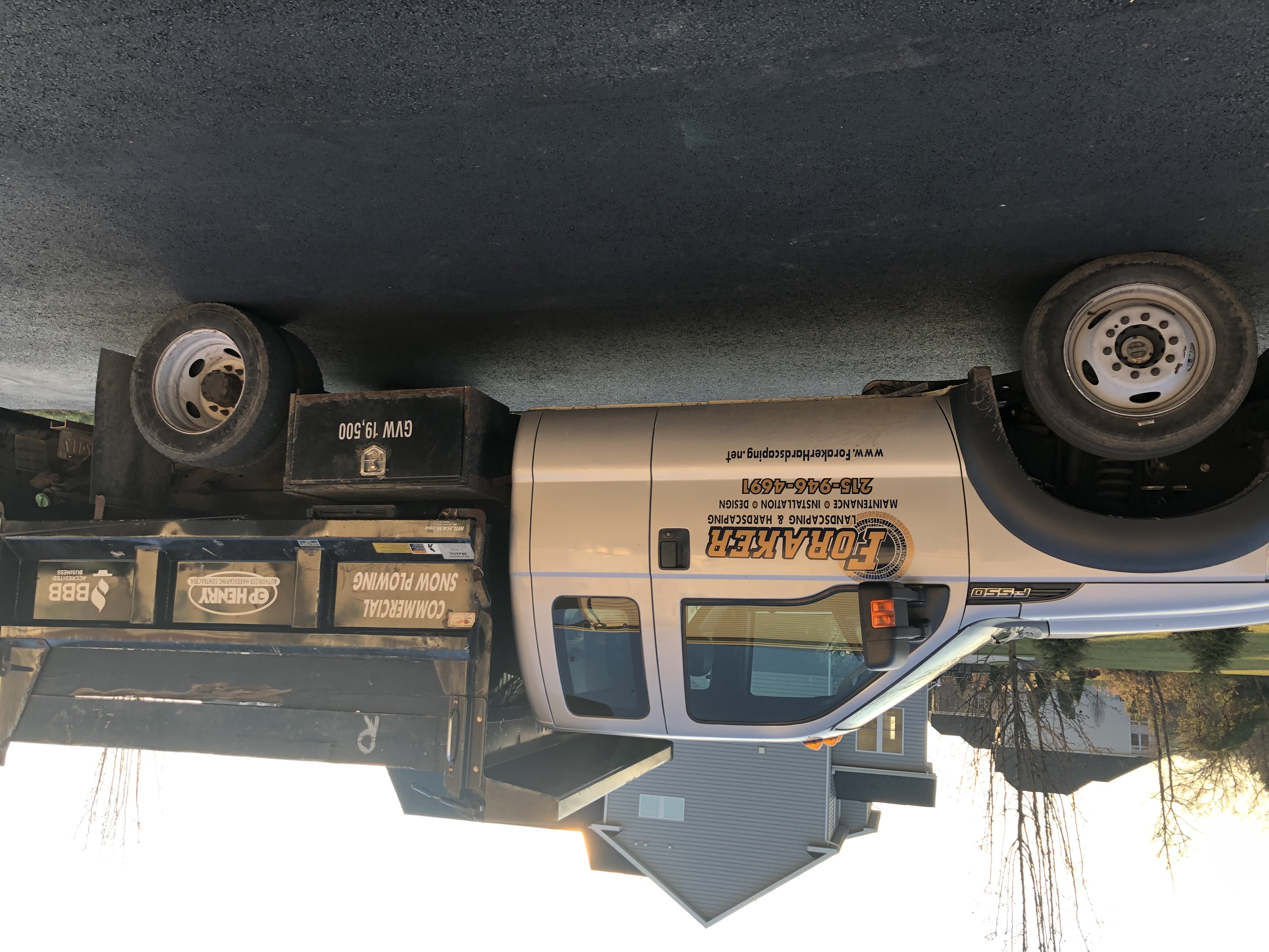 Foraker Landscaping bulk mulch delivery truck arriving at Bucks County PA residential property – brown mulch pile on driveway surrounded by green trees