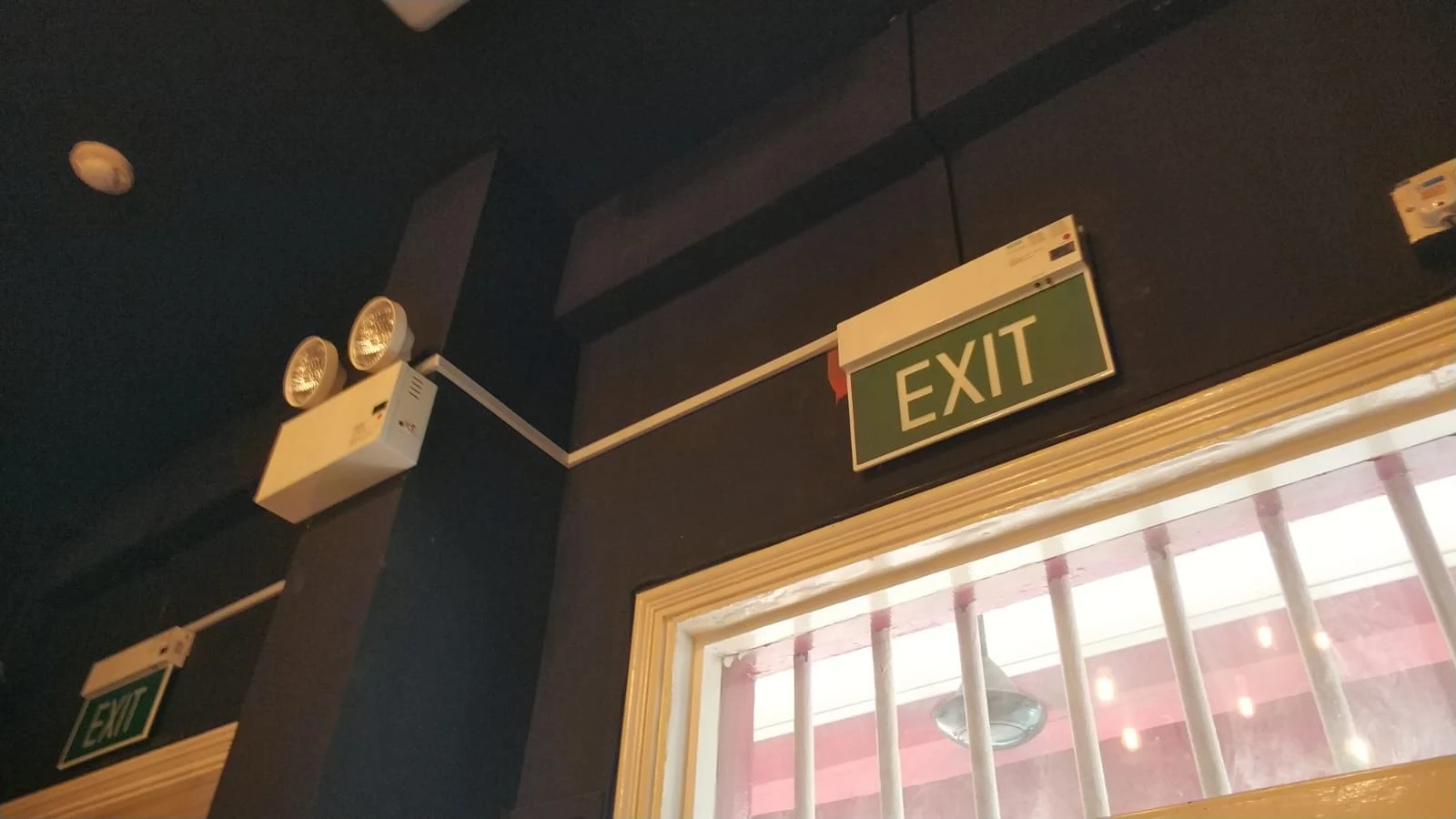 Green EXIT sign and emergency lights installed on dark wall near window